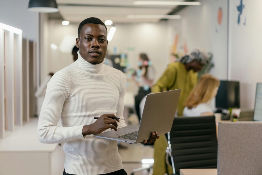 man holding a laptop with one hand, with other employees in the background
