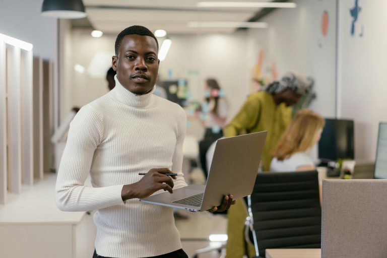 man holding a laptop with one hand, with other employees in the background