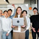 manager holding a laptop with her team members cheering behind her