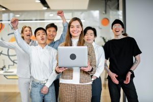 manager holding a laptop with her team members cheering behind her