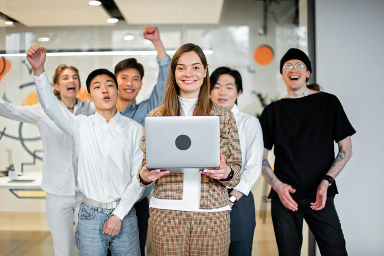 manager holding a laptop with her team members cheering behind her